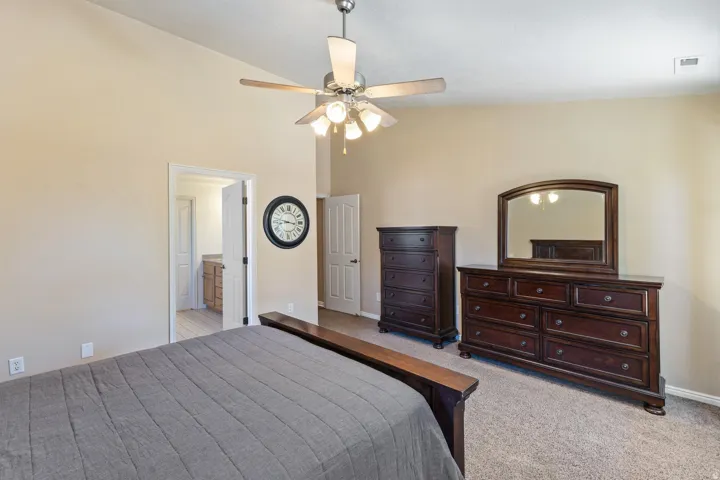 Vaulted ceiling with a ceiling fan, neutral wall tones, carpeted flooring, and a doorway leading to an additional space featuring wood-finish flooring
