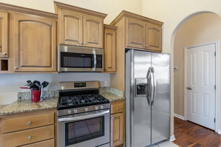 Stainless steel appliance suite, light wood-finish cabinetry, granite countertops, and arched doorway