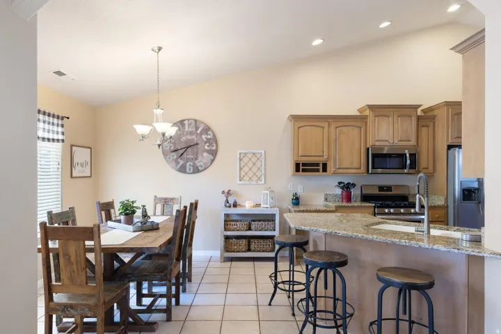 Vaulted ceilings with recessed lighting, tile flooring, wood-finish cabinetry, stainless steel appliances, and a breakfast bar with stone countertops