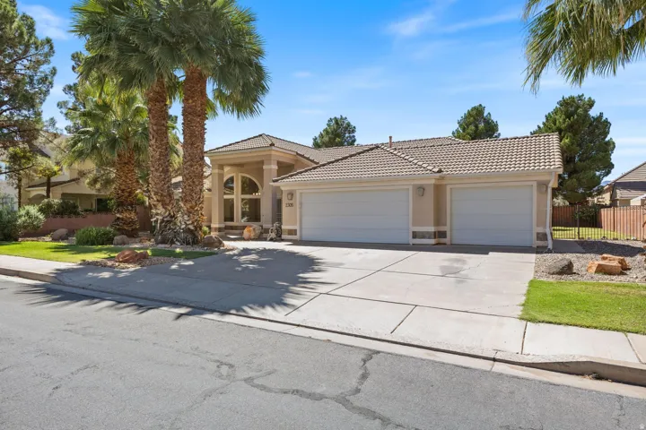 Stucco exterior with a tiled roof, multiple palm trees, a two-car garage, and a concrete driveway