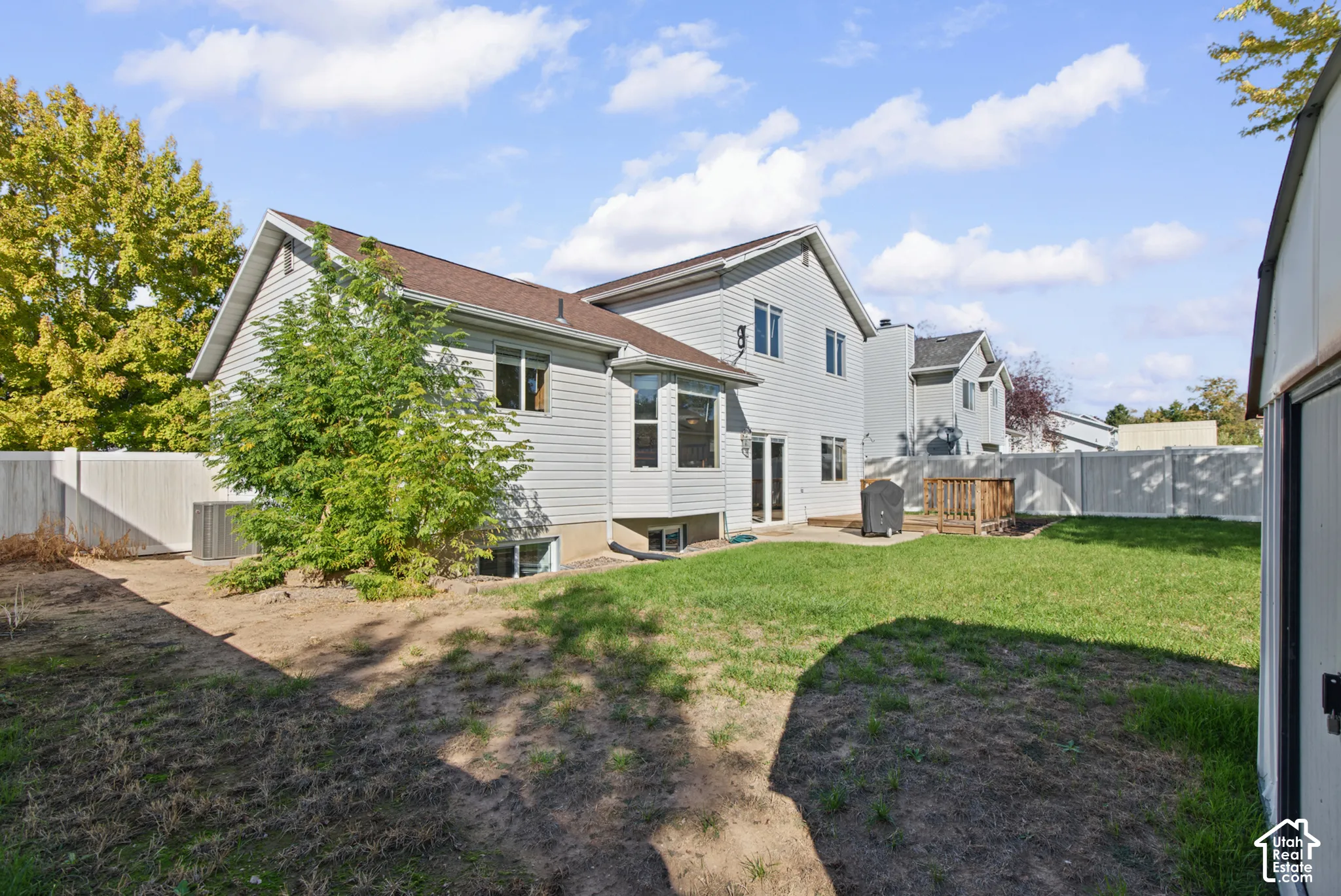 Rear exterior featuring light-toned siding, a brown shingled roof, a wooden deck, and a green lawn