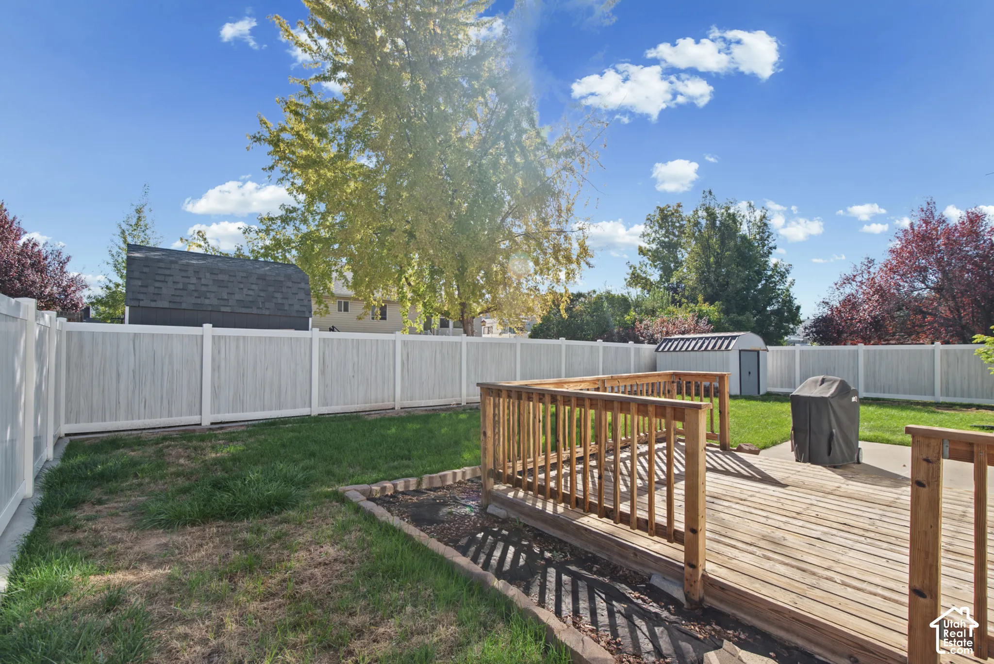 Expansive backyard featuring a wood-finish deck, manicured lawn, and white privacy fencing
