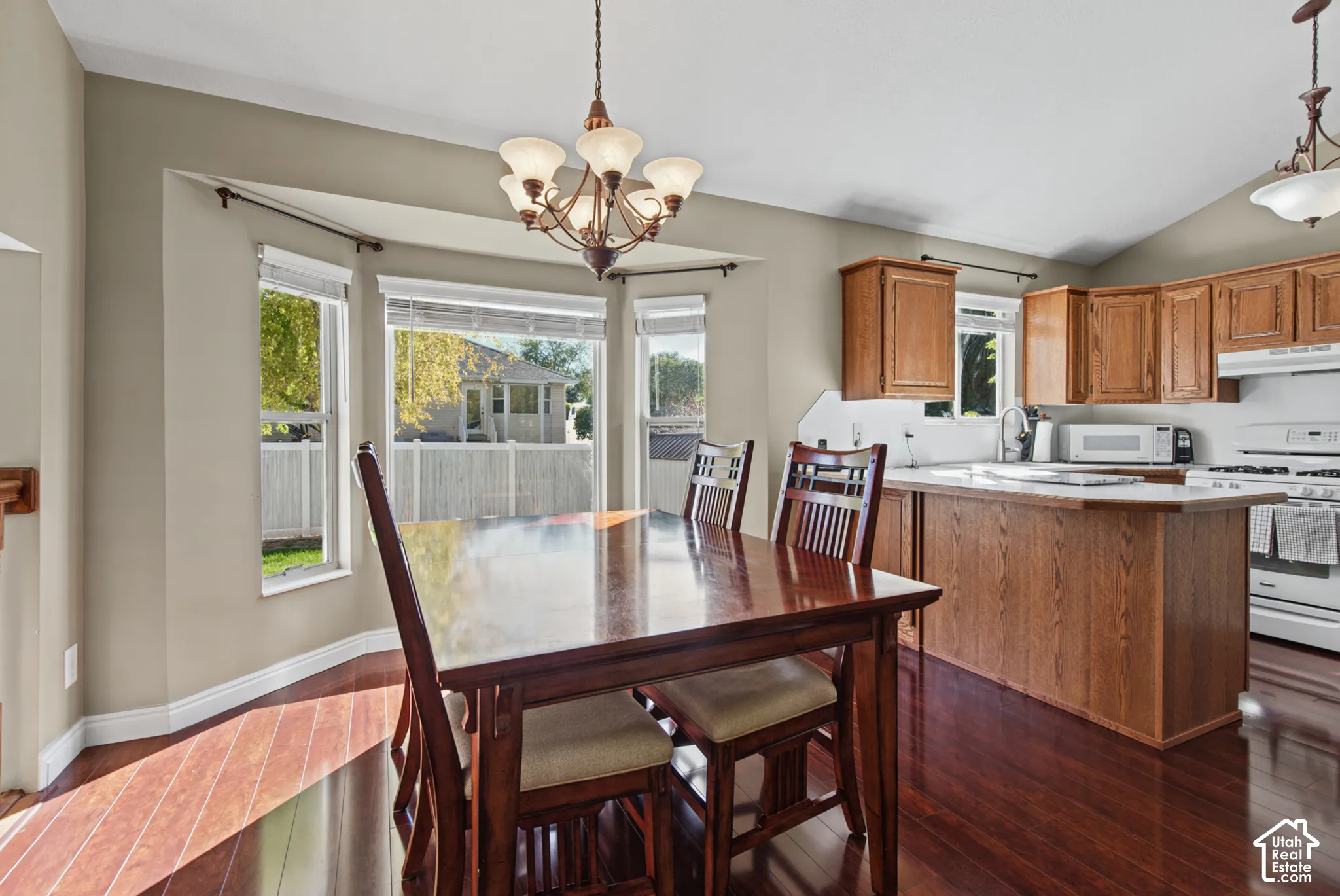 Kitchen featuring wood-finish flooring, wood cabinetry, white appliances, and a peninsula with countertop seating