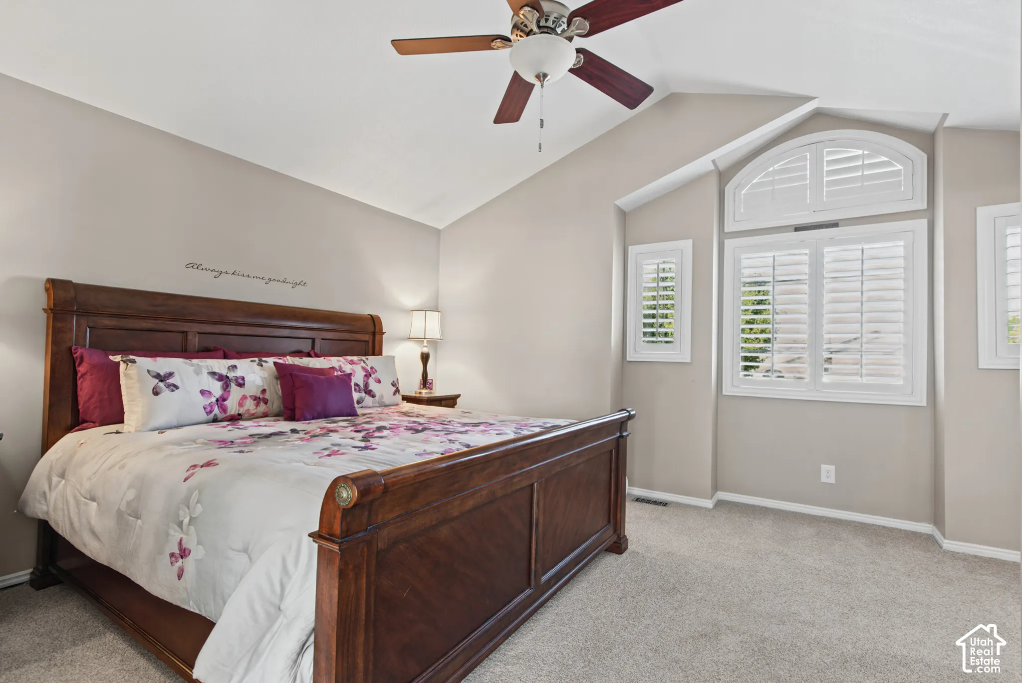 Vaulted ceiling featuring a ceiling fan with light, arched window with plantation shutters, additional windows with plantation shutters, and light-toned carpeting