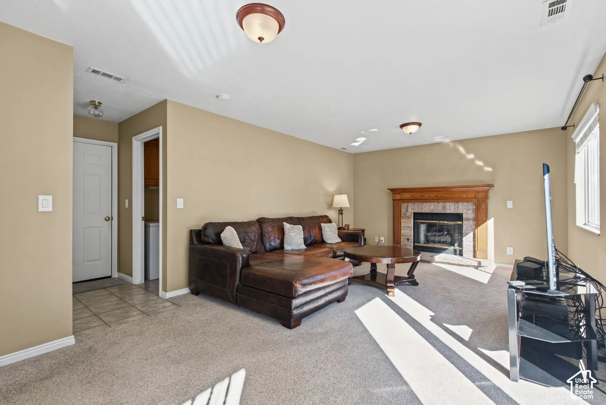 Carpeted living area featuring a fireplace with a wood mantle and tile surround, recessed lighting, and a window with blinds