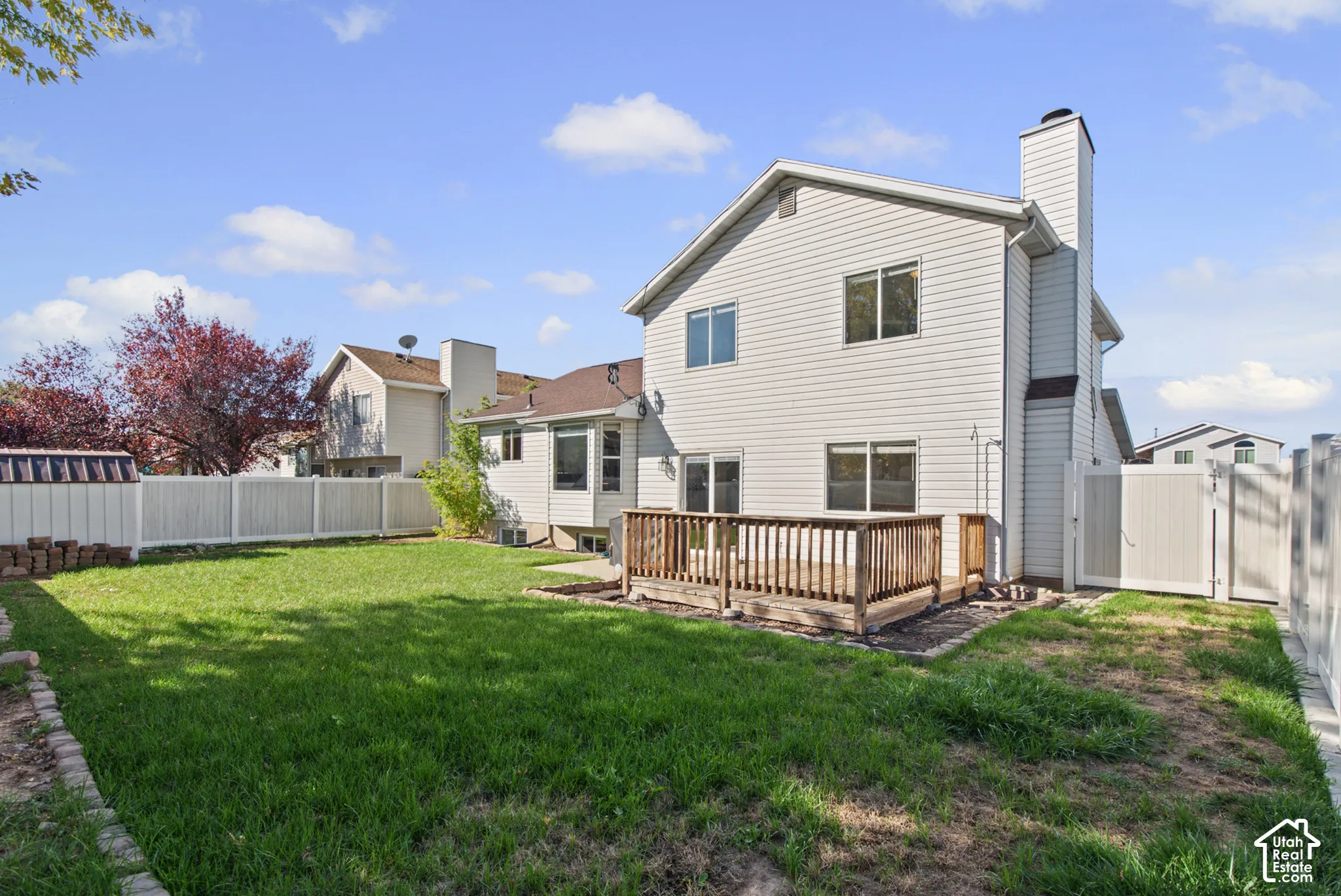 Expansive backyard featuring a wood deck, white privacy fencing, and a white siding exterior with a prominent chimney