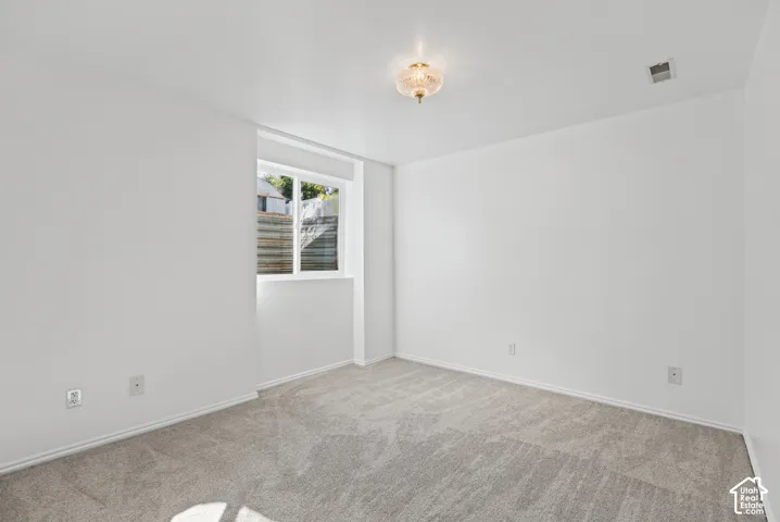 Neutral-toned walls, plush carpet flooring, a window providing natural light, and a ceiling-mounted light fixture