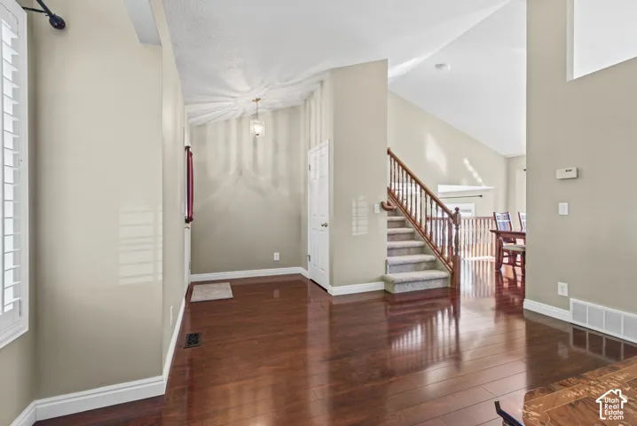 Hardwood-finish flooring, staircase with wood banister and carpeted treads, vaulted ceiling, plantation shutters, and a chandelier