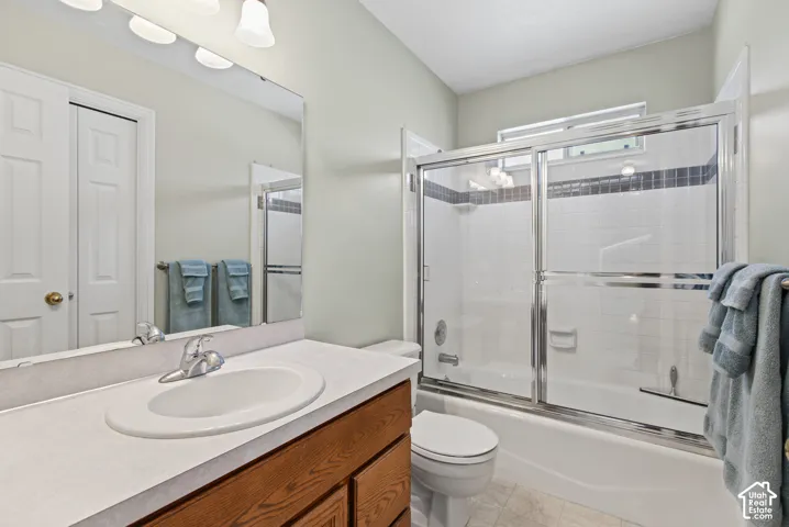 Bathroom featuring a wood-finish vanity with an integrated sink, a large mirror, and a combination tub and shower with sliding glass doors