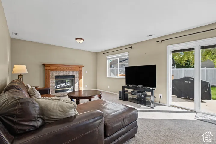 Carpeted living area featuring a fireplace with a stone surround and wood mantel, a large window, and sliding glass doors to the exterior