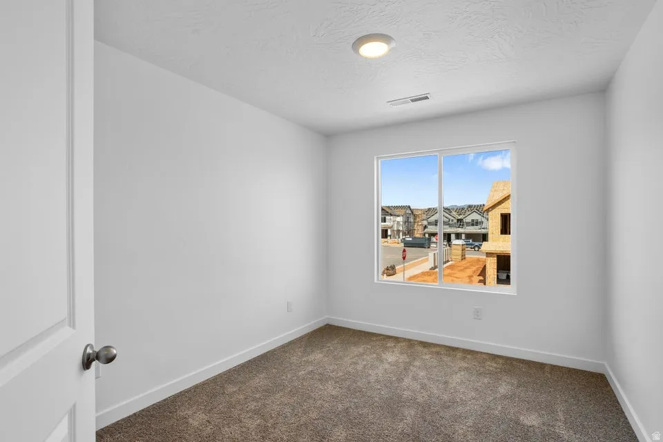 Bright interior with white walls, a single pane window, flush-mount ceiling light, and neutral-toned carpet flooring