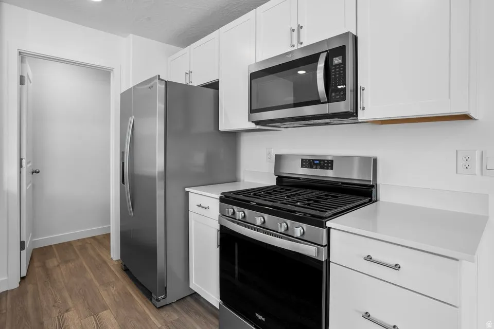 Kitchen featuring wood-finish flooring, white cabinetry, stainless steel appliances, white countertops, and a built-in microwave