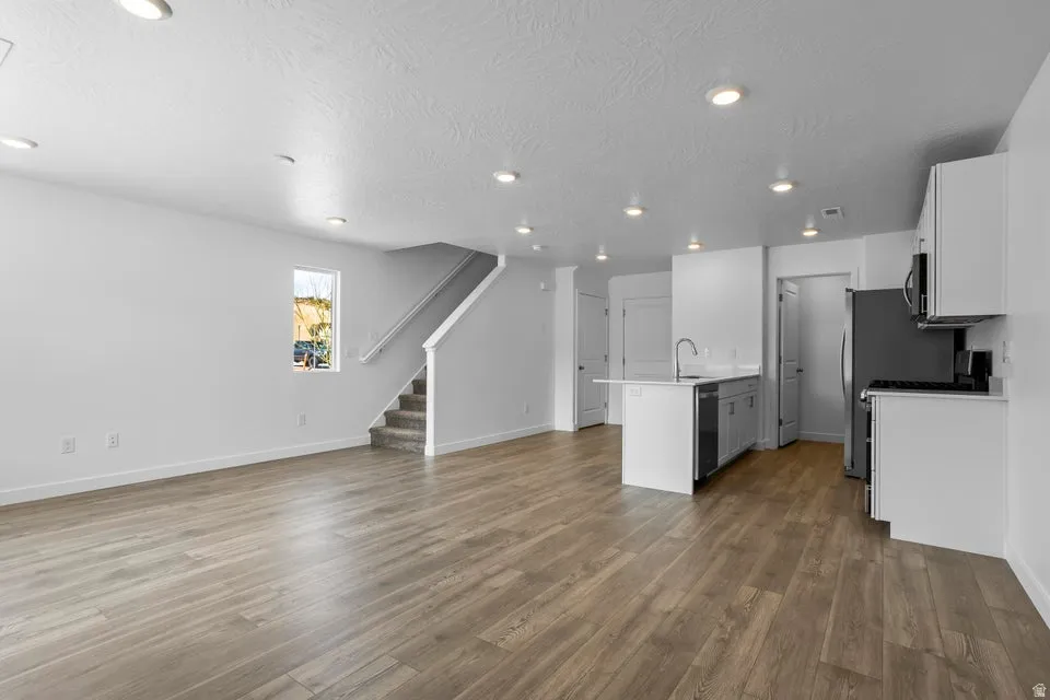 Open-concept living space featuring wood-finish flooring, recessed lighting, a kitchen island with a sink, and stainless steel appliances