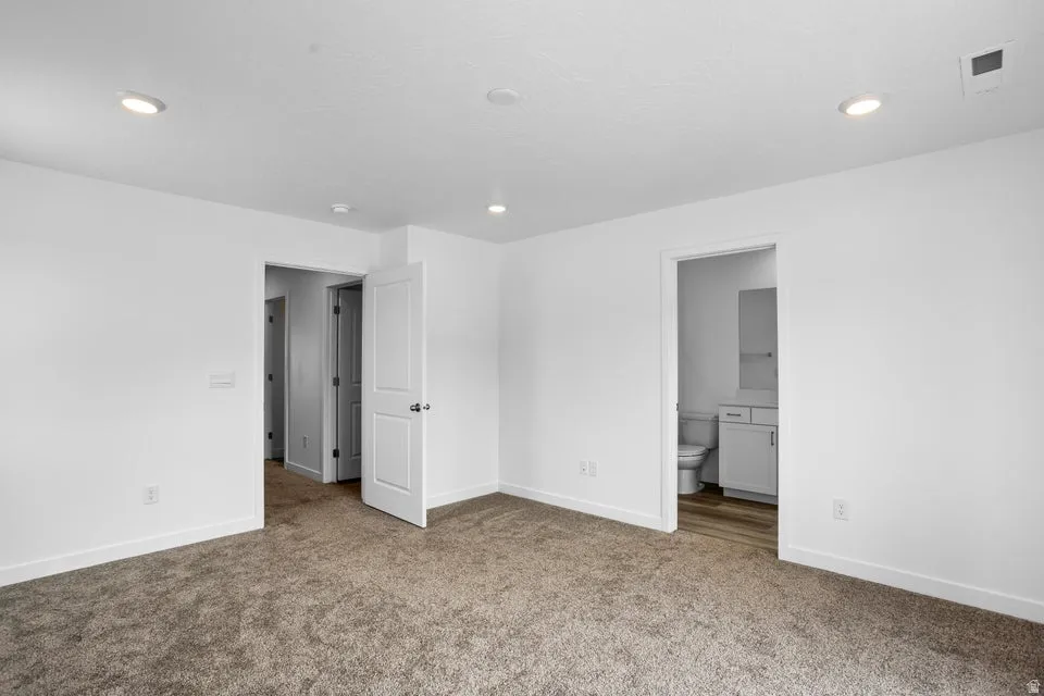 Recessed ceiling lighting, white interior walls, carpet flooring, flat panel interior doors, and a bathroom with wood-finish flooring