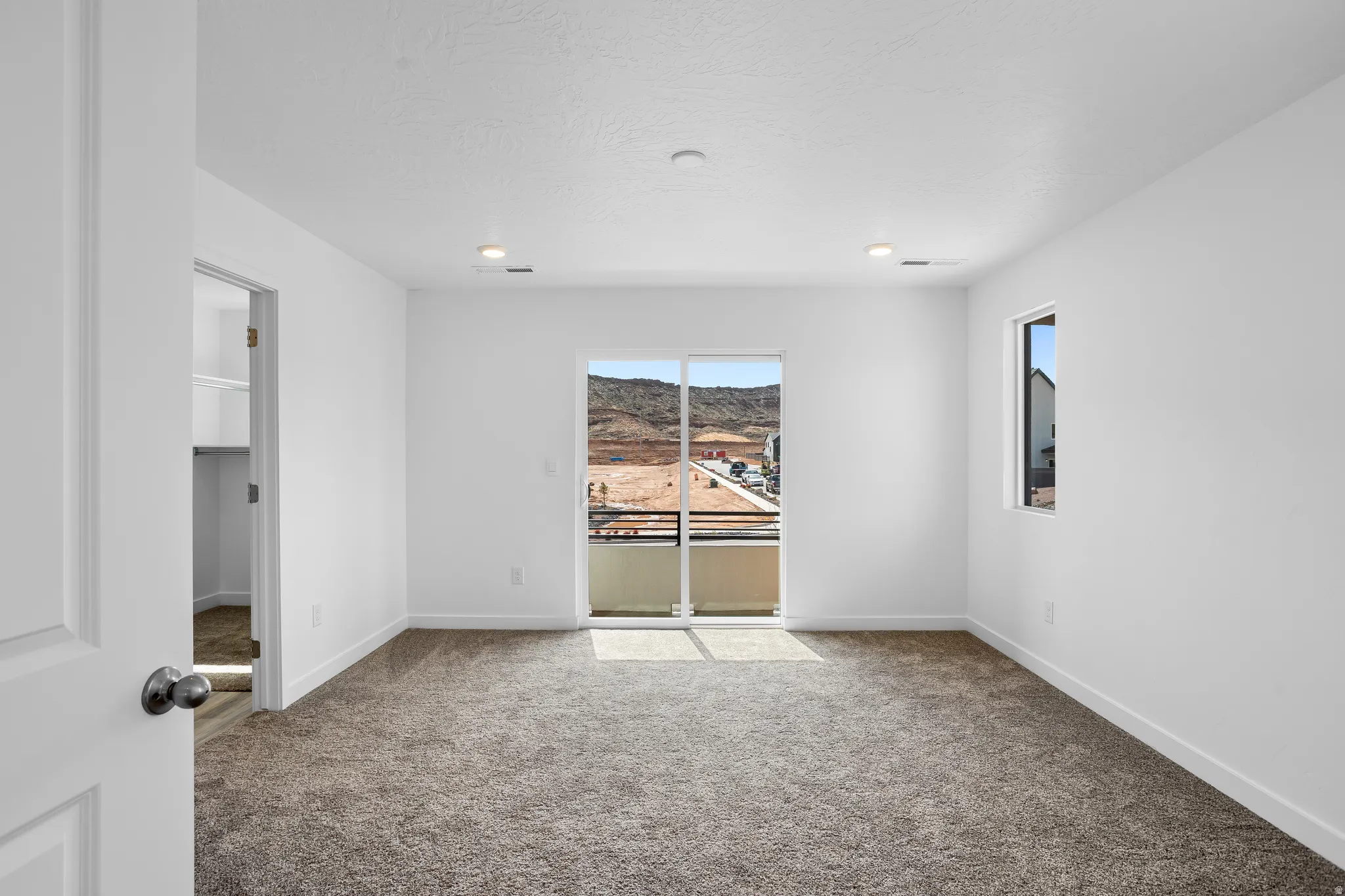 Spacious room featuring neutral carpeting, a built-in closet with shelving, a large sliding glass door to a balcony, and a secondary window
