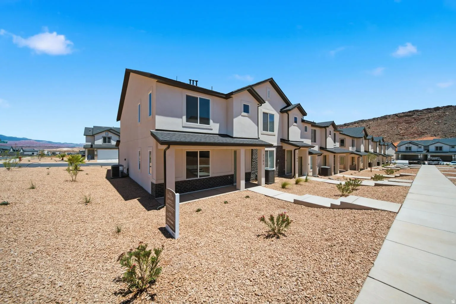 Contemporary townhome featuring a neutral stucco exterior, dark roof, prominent windows, and a covered entry