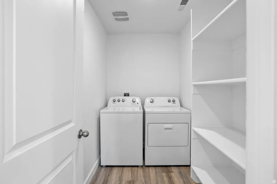 Laundry area featuring wood-finish flooring, white built-in shelving, and white walls