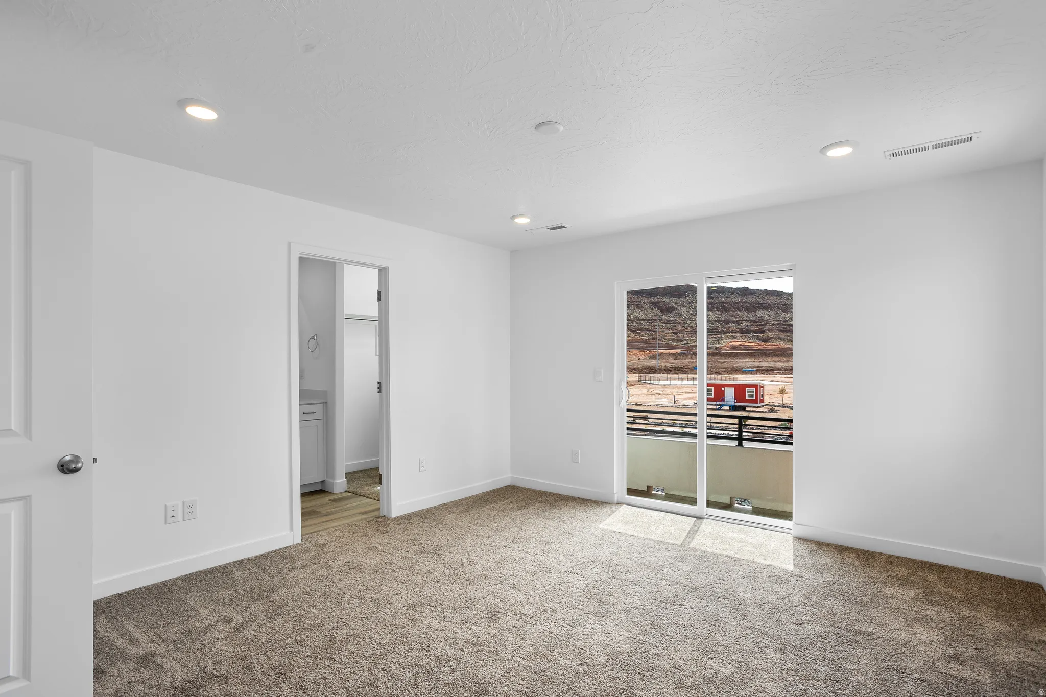 Plush carpeted flooring, recessed lighting, and a sliding glass door leading to an outdoor balcony