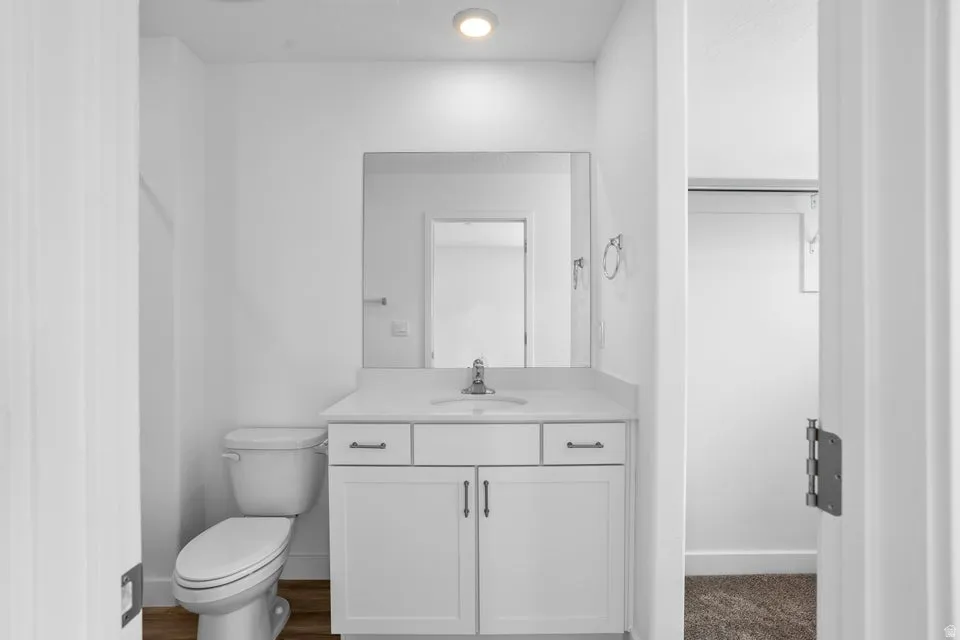 Bathroom featuring a single vanity with storage, an integrated sink, a large mirror, and wood-finish flooring