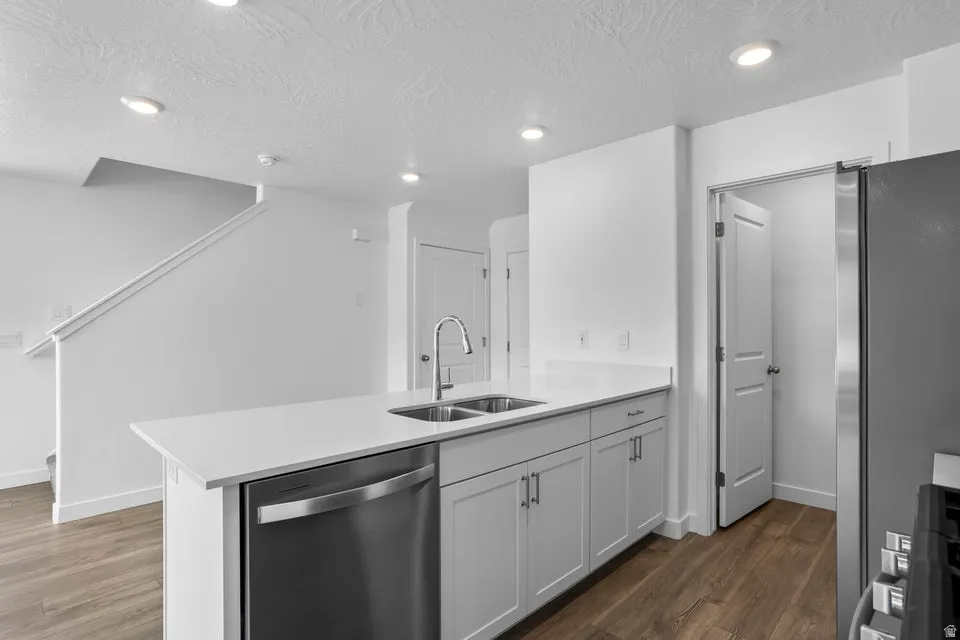 Kitchen island featuring white countertops, an undermount double basin sink with a gooseneck faucet, light gray cabinetry, and a built-in stainless steel dishwasher