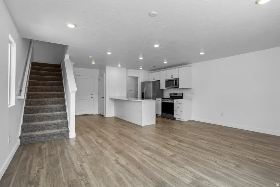 Open-concept living area featuring wood-finish flooring, recessed lighting, and a kitchen with white cabinetry and stainless steel appliances