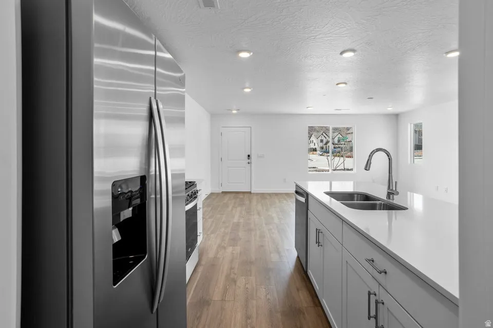 Kitchen featuring stainless steel appliances, wood-finish flooring, recessed lighting, and a center island with a double basin sink and gooseneck faucet