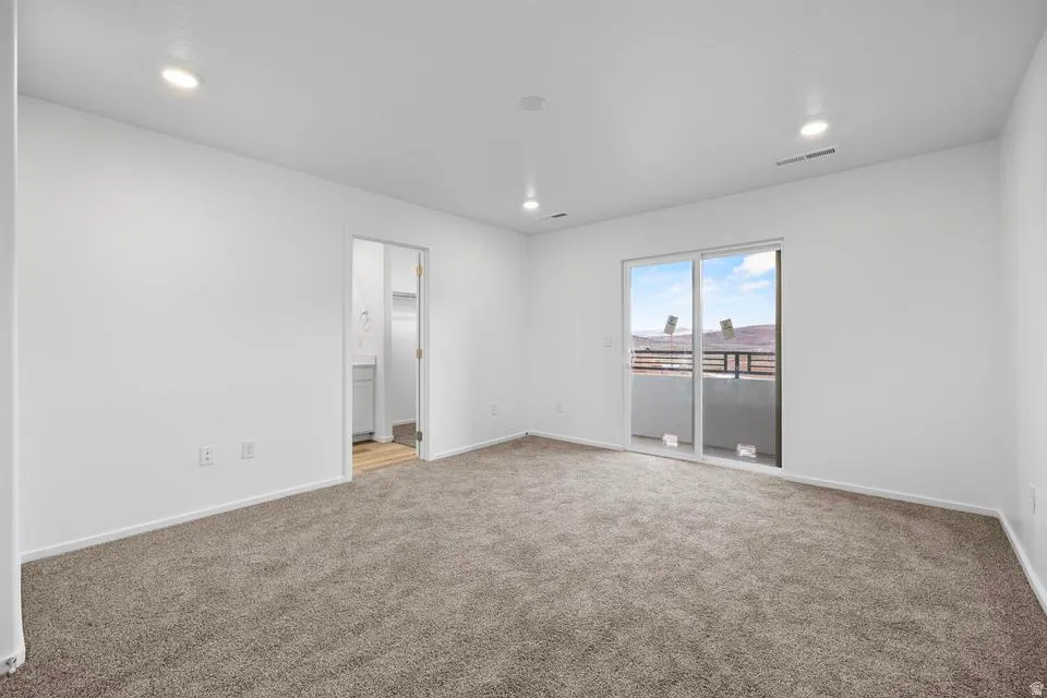 Recessed lighting, light-toned carpeting, white walls, and a sliding glass door opening to an outdoor area