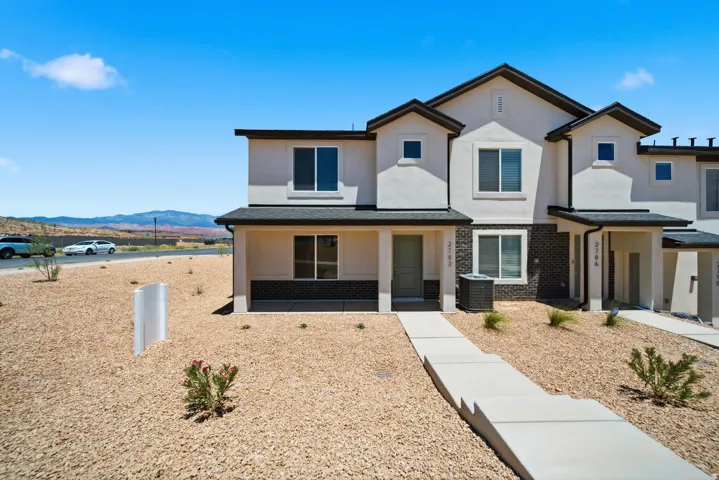 Contemporary two-story exterior with stucco and dark brick accents, covered front entry, and a concrete walkway