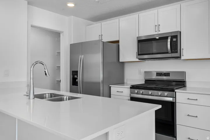 White cabinetry, stainless steel appliances, dual basin sink, and solid surface countertops