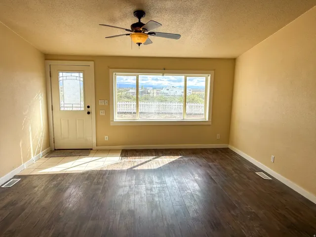 Wood-finish flooring, ceiling fan with light fixture, large window with outdoor scenery, front door with decorative glass inserts, and tile entry