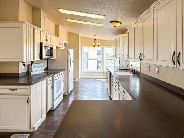 Kitchen featuring light-toned cabinetry, dark countertops, a built-in microwave, and a double-basin sink with a gooseneck faucet