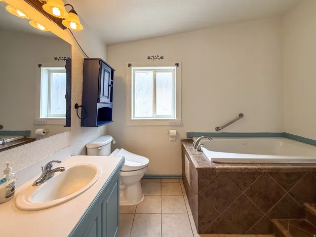 Tiled flooring leading to a built-in jetted tub with tiled surround, a window, and an integrated grab bar