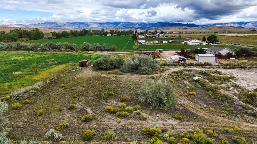 Expansive rural property featuring an outbuilding and diverse vegetation, with multiple structures and cultivated fields in the background, all set against a backdrop of distant mountains