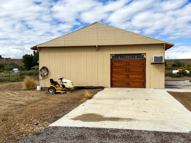 Detached garage structure with a pitched roof, vertical siding, an overhead wood-finish garage door with window inserts, and an exterior mounted unit