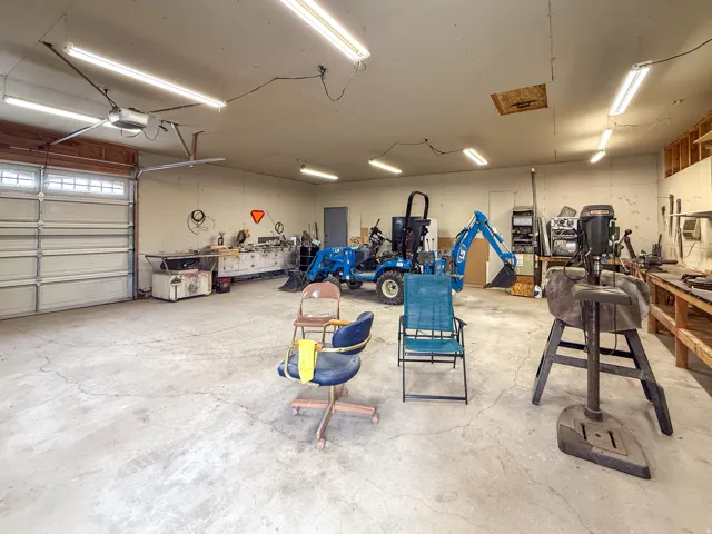 Expansive garage with concrete flooring, multiple fluorescent lighting fixtures, large overhead door with transom windows, and a ceiling-mounted fan