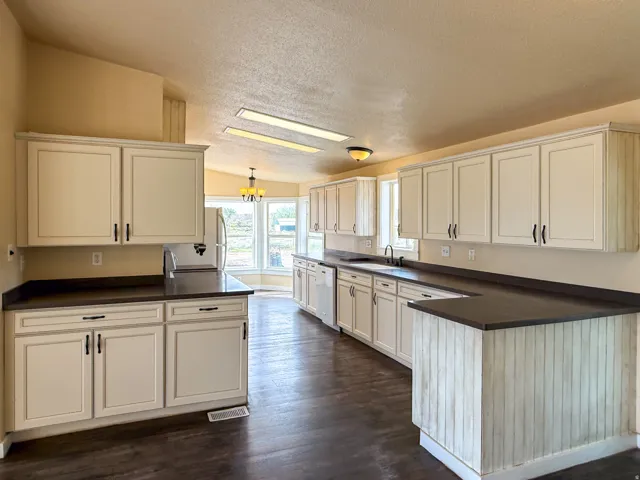 Kitchen featuring extensive cabinetry, dark countertops, wood-finish flooring, recessed lighting, and a built-in dishwasher