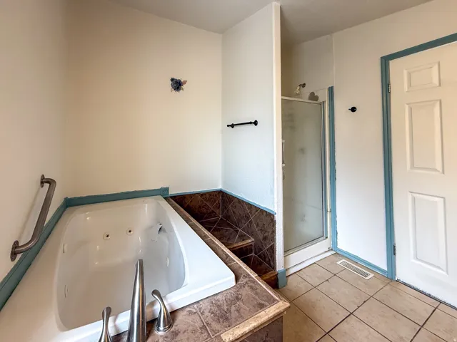 Built-in jetted tub with grab bar, brushed nickel fixtures, and tiled surround