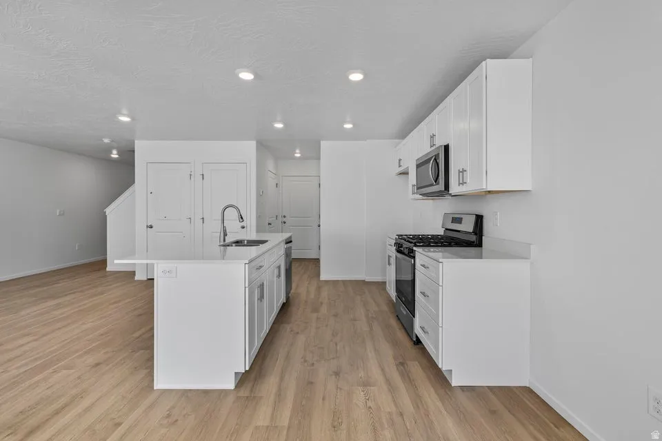 Kitchen featuring a center island with sink, white shaker cabinetry, stainless steel appliances, and light wood-finish flooring