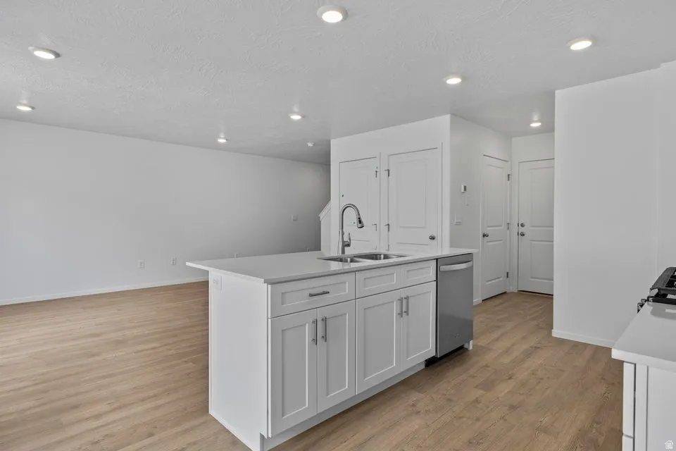 Kitchen island with an undermount sink, gooseneck faucet, white shaker cabinetry, and a built-in dishwasher