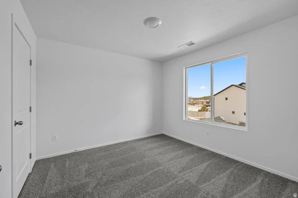Spacious room featuring gray patterned carpeting, white walls, a large window, and a white interior door with black hardware