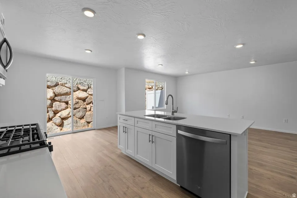 Open-concept kitchen featuring an island with a stainless steel sink and dishwasher, a gas range, recessed lighting, and wood-finish flooring