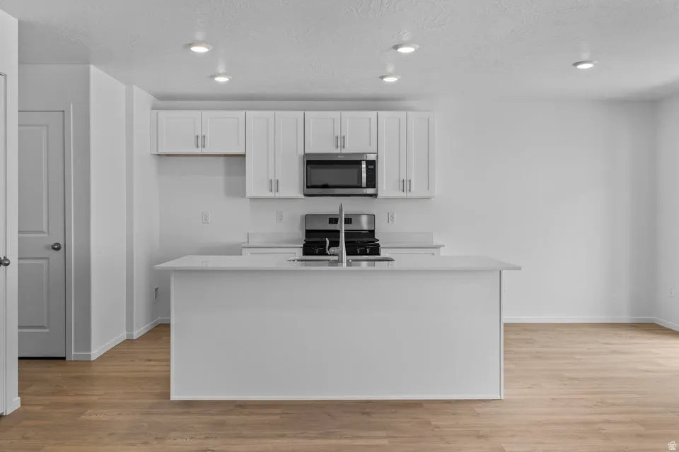Kitchen featuring white shaker cabinetry, stainless steel appliances, quartz countertops, a kitchen island with an undermount sink, and recessed lighting