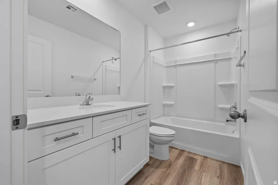 White vanity with a neutral-toned countertop and an integrated sink, wood-finish flooring, and a white tub and shower surround