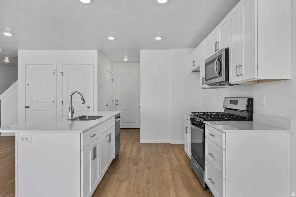 Kitchen featuring white cabinetry, stainless steel appliances, wood-finish flooring, recessed lighting, and a kitchen island with a stainless steel sink