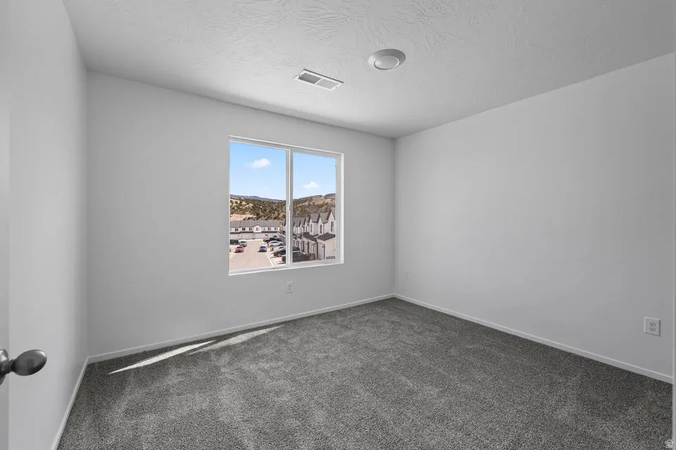 Neutral wall tones, gray carpeting, recessed ceiling light, and a window with exterior scenery