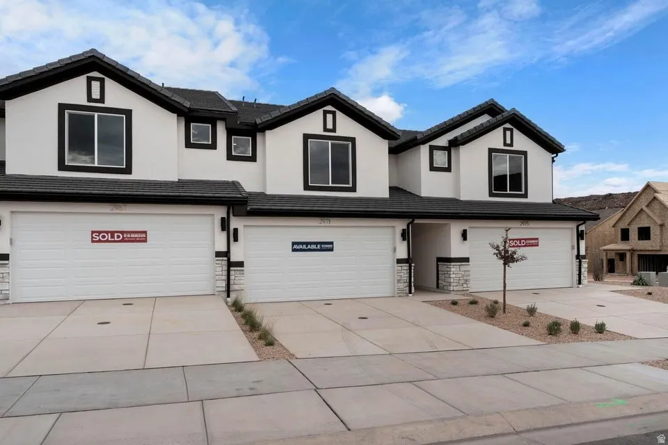 White stucco exterior with black trim windows, multi-pane windows, black asphalt shingle roof, integrated single-car garages, and concrete driveways
