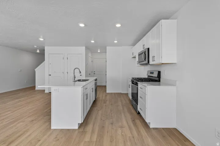 Kitchen featuring a center island with sink, white shaker cabinetry, stainless steel appliances, and light wood-finish flooring