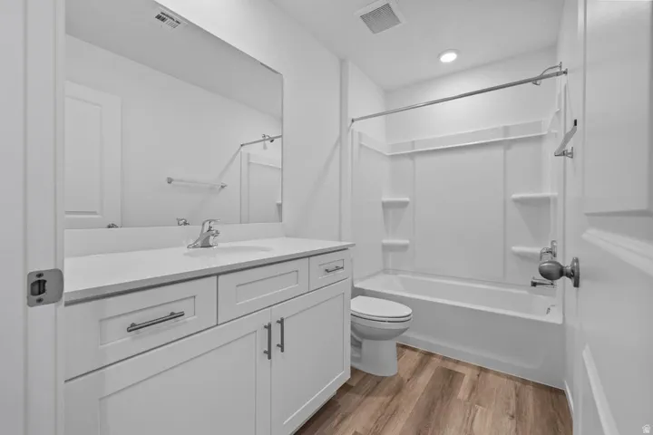 White vanity with a neutral-toned countertop and an integrated sink, wood-finish flooring, and a white tub and shower surround