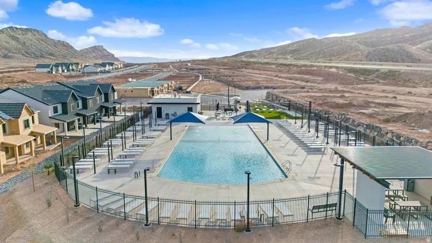 Community swimming pool with an expansive concrete deck, shaded seating areas, and a surrounding security fence