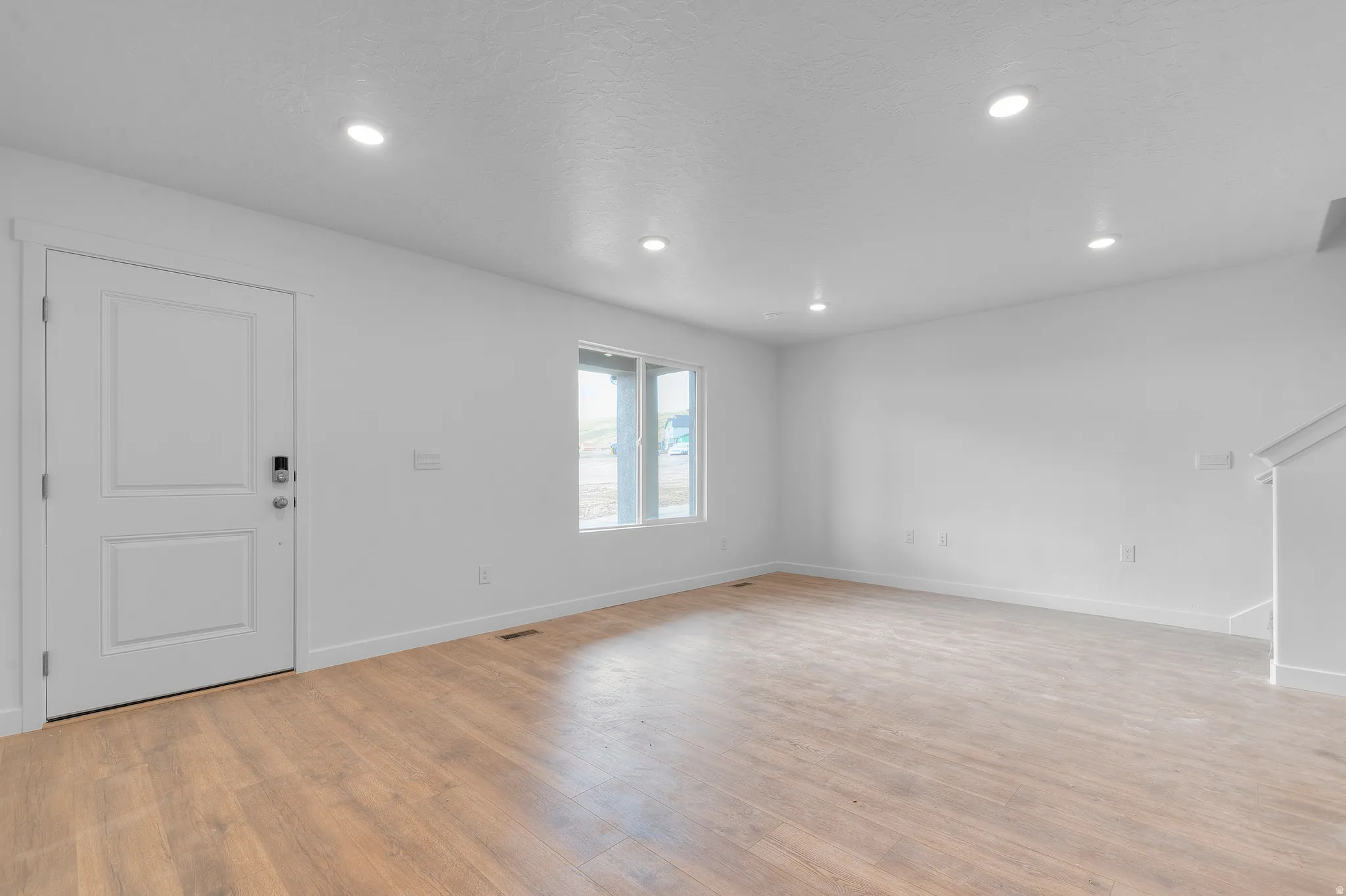 Spacious room featuring wood-finish flooring, recessed lighting, and a window for natural illumination